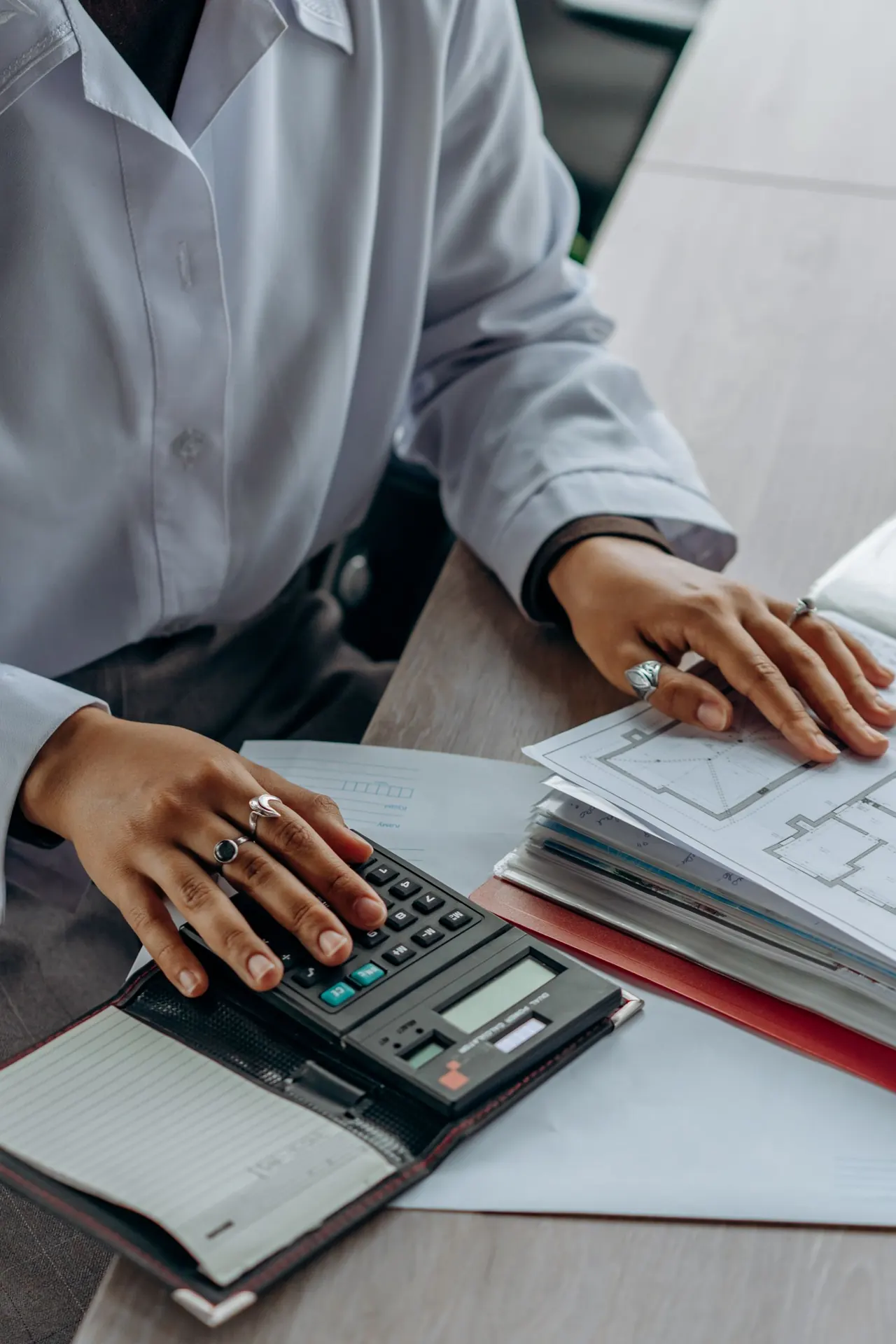 Hands totalling figures on a calculator beside a stack of documents